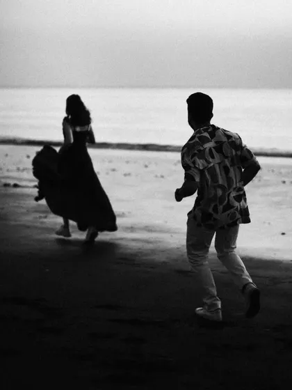 A black and white action shot of a couple running on the beach, creating a sense of cinematic drama. This moody photograph captures a story in motion.