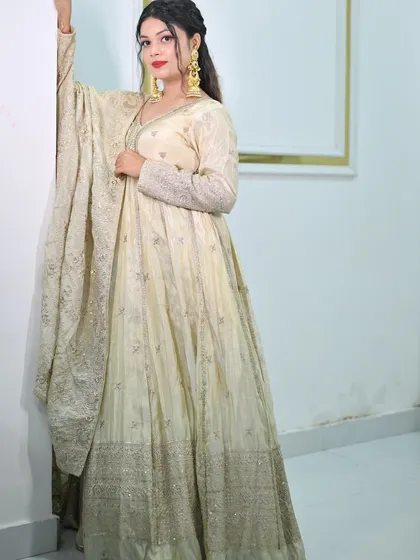 A model posing against a white wall in the ivory anarkali gown, highlighting the elegant V-neck and embellished sleeves.