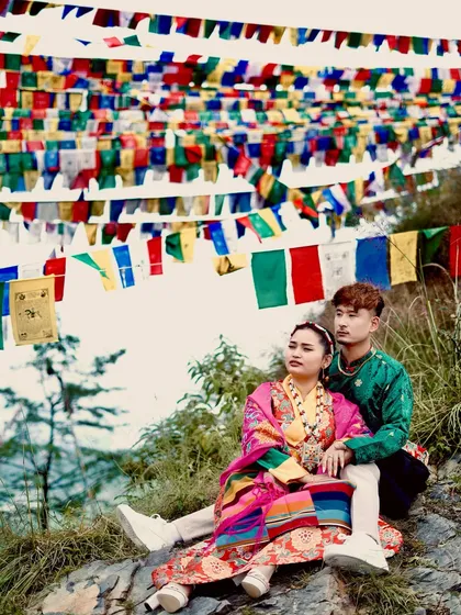 A couple's portrait celebrating traditional Kinnauri attire against a backdrop of vibrant Buddhist prayer flags. This kind of cultural photoshoot is special to me and highlights the rich heritage of Himachal.