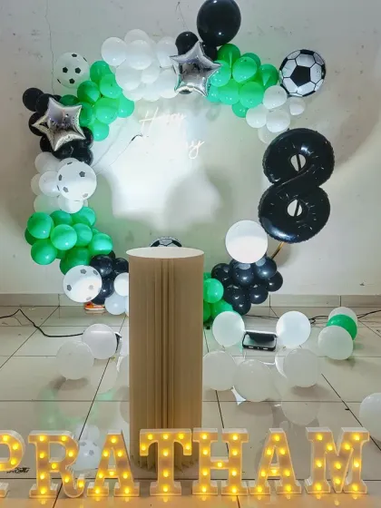 A football-themed 8th birthday with a circular balloon arch. The green, white, and black balloons are accented with football foil balloons and a light-up number '8'.