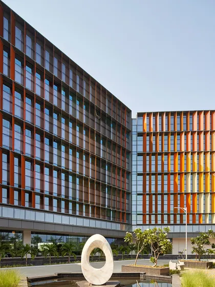The exterior of the Infosys Nagpur campus, showing the interplay between the colourful facade, the surrounding landscape, and a sculptural art piece. The design integrates art and architecture to create a holistic and inspiring environment.