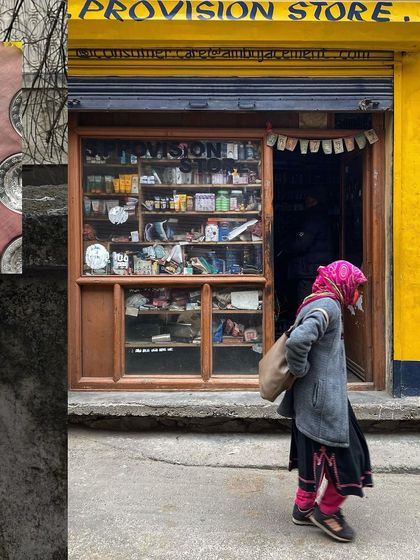 A striking image of a woman in a pink headscarf walking past a yellow provision store.