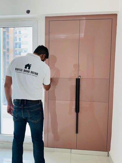 A close-up of a wardrobe with a glossy pink laminate finish and elegant long handles.