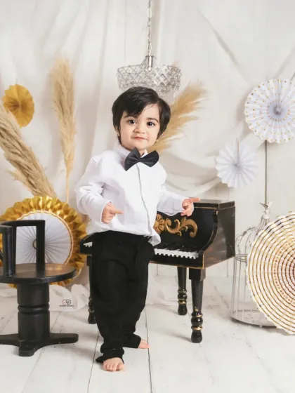 A dapper little gentleman dressed in a bow tie for his 'Pianist' themed session. He poses with a miniature piano, creating a classic and charming toddler portrait.