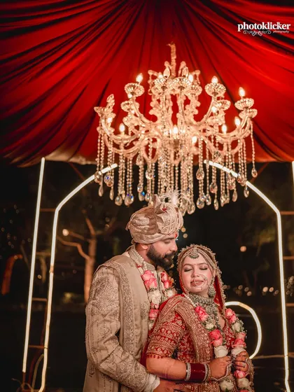 An intimate shot of the couple during their Jaimala ceremony, framed by a magnificent crystal chandelier that adds to the grandeur of the moment.