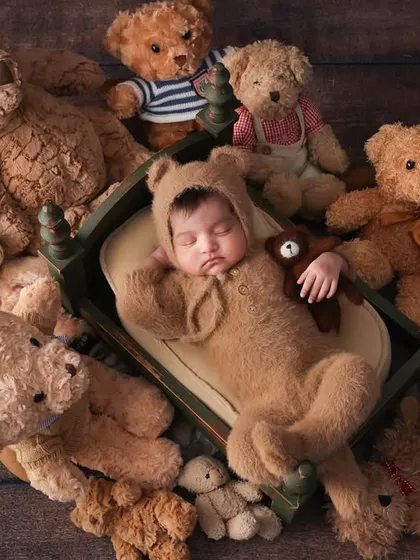 Dreaming among the teddies. This adorable setup features a newborn dressed as a tiny bear, sleeping soundly on a miniature bed surrounded by fluffy friends. It’s a heartwarming theme that is always a favorite.