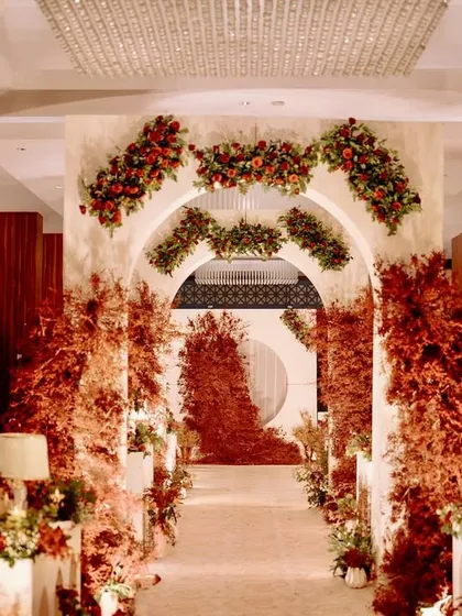 A dramatic and romantic reception entrance, with a long aisle flanked by modern white arches and explosive arrangements of red foliage, leading to a stunning focal point.