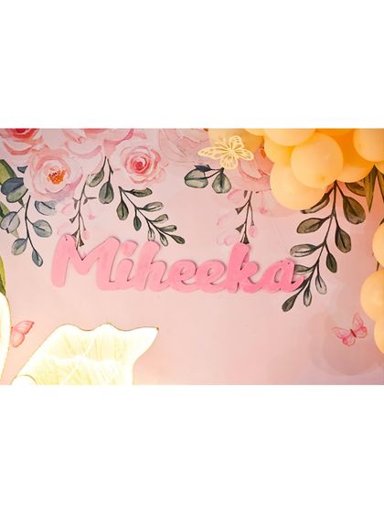 A personalized 'Miheeka' name sign in pink, set against a beautiful floral and butterfly backdrop, adding a custom touch to the party decor.