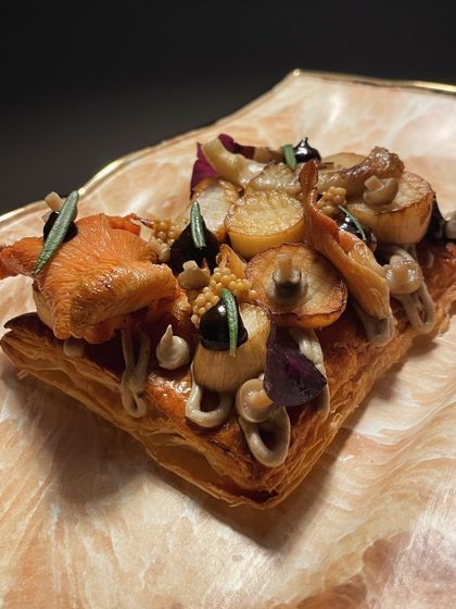 A creative mushroom tartine on a flaky pâte feuilletée base. It's topped with black garlic ketchup, mushroom mascarpone, and a variety of wild mushrooms.
