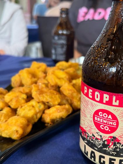 Enjoying a cold lager from Goa Brewing Co. with some crispy fried snacks. This shot captures the relaxed, 'susegad' vibe of a Goan monsoon trip, blending local products with a vacation feel.