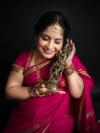 A close-up shot against a dark background, making the vibrant pink saree and the mother's joyful expression the complete focus. This is a perfect example of a traditional maternity portrait.