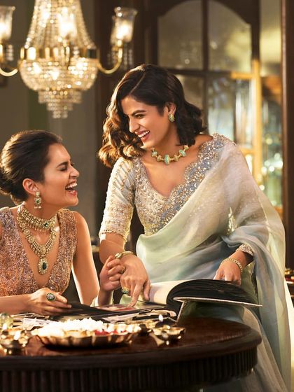 Two women sharing a laugh in this scene for a Tanishq campaign. The styling uses soft, elegant sarees and distinct jewellery sets for each model, showcasing different pieces from the collection within a single, relatable narrative.