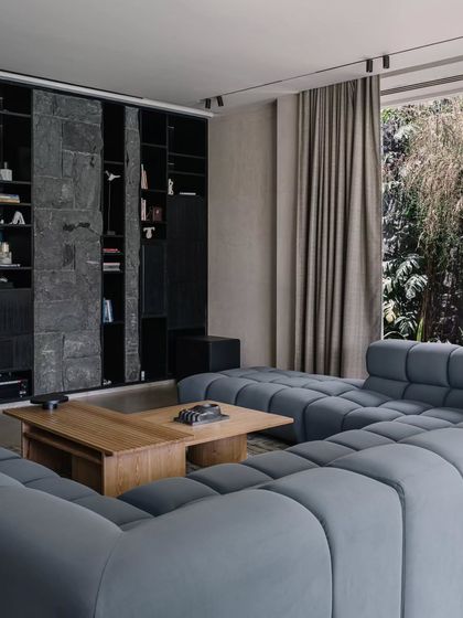 The entertainment lounge, with its large modular sofa, is designed for casual movie nights. The bookshelf is made of black stone, adding a touch of earthy sophistication to the room.