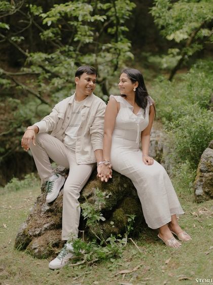 A relaxed and happy portrait of the couple sitting on a mossy rock in the forest, holding hands and sharing a smile.