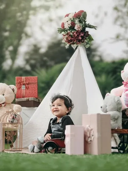 A happy moment from an outdoor first birthday shoot. The natural setting and classic props like the teepee and teddy bears create a timeless portrait.