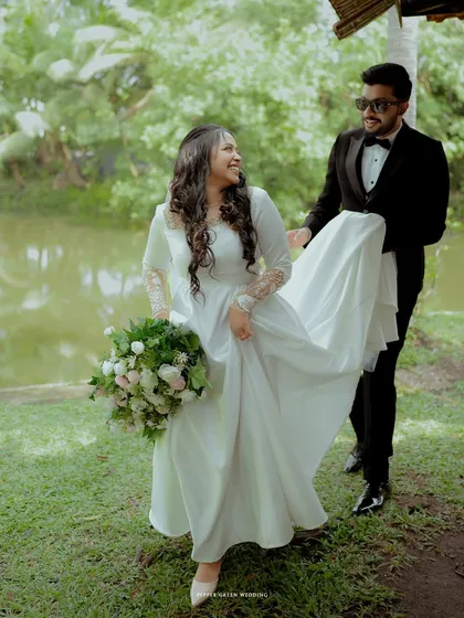 A playful moment as the groom lifts the bride's dress as they walk, creating a sense of fun and movement in this garden wedding portrait.
