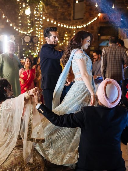 A fun moment on the dance floor as a guest helps the bride with her lehenga while she dances.