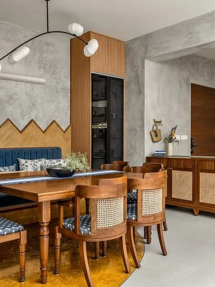 This dining area showcases several custom pieces, from the bench seating with its geometric wood-paneled backdrop to the cane-fronted sideboard. The color palette of turmeric yellow and grey adds a unique vibrancy.