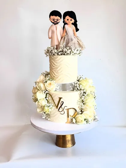 A studio shot of the engagement cake, showing the handcrafted couple topper and the beautiful arrangement of white roses.