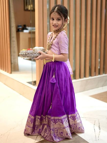 A full-length view of the custom purple pattu pavadai, showing the beautiful zari border on the skirt and the delicate tassels.