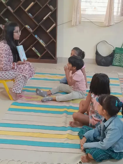 A small group of children listens to a story about a monkey, told with puppets and a book.