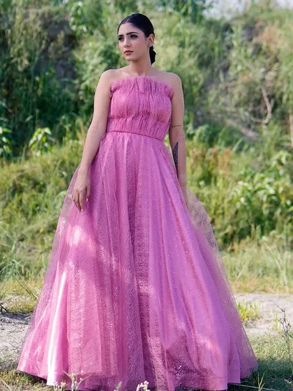 A full-length shot of a model standing in a field, wearing a beautiful pink strapless gown. The contrast between the vibrant pink and the natural green background makes the image pop.