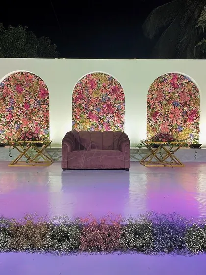 A modern and chic reception stage design. The clean white arches filled with vibrant pink and lilac floral panels, paired with hanging cage chandeliers, created such a fresh and stylish look.