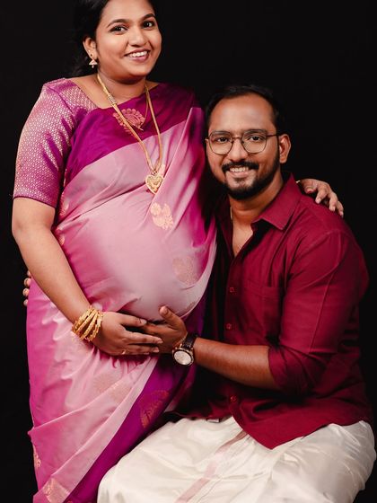 A joyful and warm traditional portrait. The dad-to-be kneels to lovingly hold the baby bump, and their smiles radiate the happiness of this special time.
