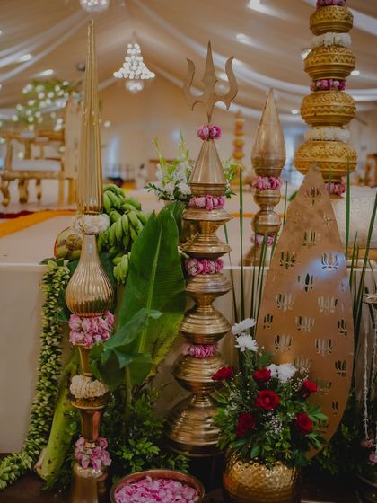 An arrangement of traditional brass decor pieces, including a Trishul (trident), surrounded by banana leaves and fresh flowers for a divine touch.