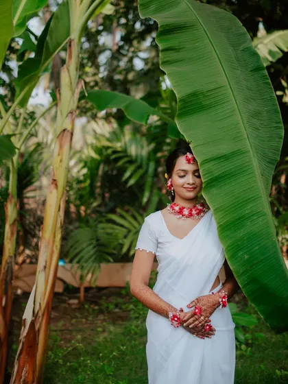 A creative bridal portrait during a Haldi ceremony, using a large banana leaf as a natural frame. This highlights the bride's serene glow against a lush, green backdrop.