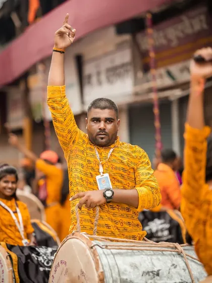 The color version of the dhol player giving a signal, the orange shirts of the troupe creating a vibrant backdrop.