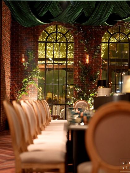 The dining setup at the glass house reception, with long tables set against arched windows and exposed brick. The design opted against a conventional approach, instead drawing inspiration from the venue itself.