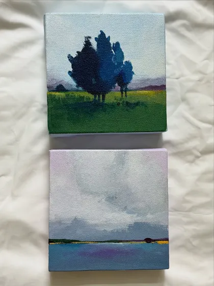 Two miniature landscape paintings, one of a moody sky over water and the other of a solitary blue tree in a field. Each small canvas captures a distinct atmosphere.