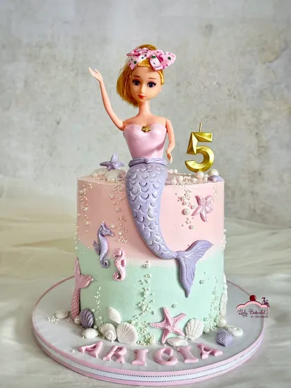 A pretty pastel mermaid doll cake for a 5th birthday. The doll's tail is part of the cake, decorated with ombre buttercream and edible shells.