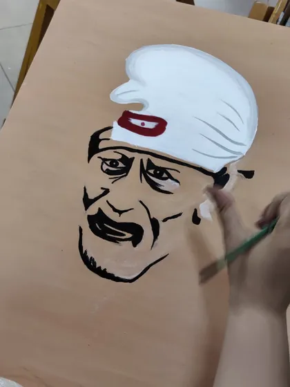 An adult student is captured through the process of painting a portrait of Sai Baba, showing concentration and devotion in his work.