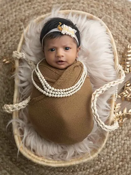 An overhead view of a newborn nestled in a basket with earthy tones and a string of pearls, showing a complete and beautifully styled setup.
