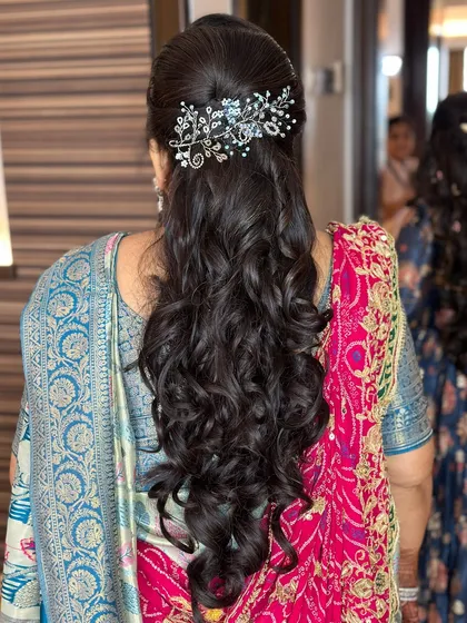 A classic half-up hairstyle with beautiful curls, created for the mother of the bride during a Haldi ceremony.
