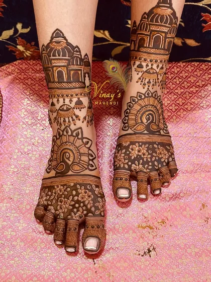 This unique bridal feet design combines palace architecture with hanging jhumkas and peacock figures, creating a festive and royal look.