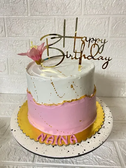 Pink and white and everything nice. This two-tone vanilla cake is accented with a fresh flower and a gold "Happy Birthday" topper.