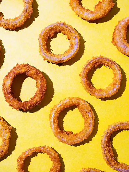 A minimalist flatlay of crispy onion rings arranged in a pattern on a bright yellow background. The hard light and simple composition create a fun and graphic image.