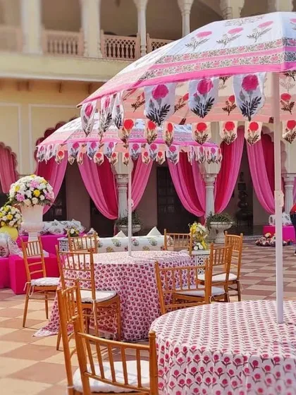 A daytime Mehendi function held in a palace courtyard, featuring decor inspired by Rajasthani block prints. The custom-printed umbrellas and tablecloths, paired with bright pink drapes, created a festive and culturally rich setting.