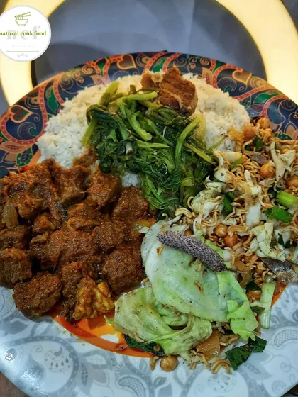 A satisfying meal of spicy buff curry, boiled mustard leaves, and a crunchy cabbage salad with noodles, served on a traditional patterned plate.