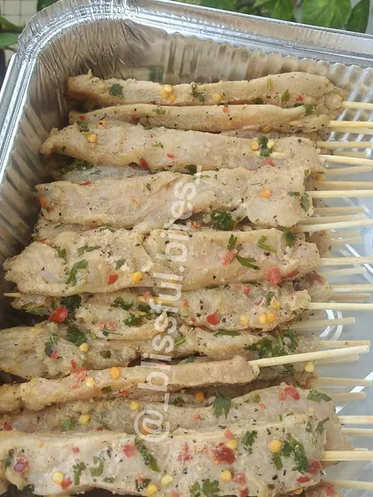A tray of uncooked Satay Chicken skewers, showing the fresh marinade of herbs and chili flakes on each tender piece of chicken.