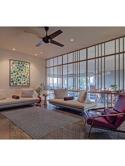 Another view of the Sky Residence, showing a more relaxed seating area. The space is defined by a metal and glass screen that separates it from the dining area without blocking light, maintaining an open and airy feel.