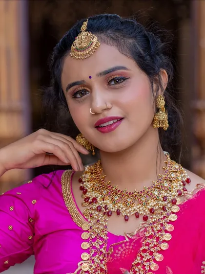 A detailed portrait showcasing the makeup and jewellery. The focus is on the clean base, defined brows, and the beautiful contrast of the pink saree with the gold jewellery.