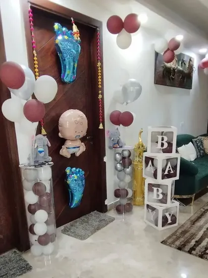 A complete view of a doorway decorated to welcome a new baby boy. The setup includes foil balloons, "BABY" blocks, and balloon pillars.