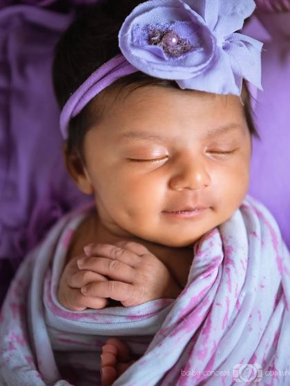 A beautiful close-up of a smiling newborn with a dimple, wearing a purple headband.