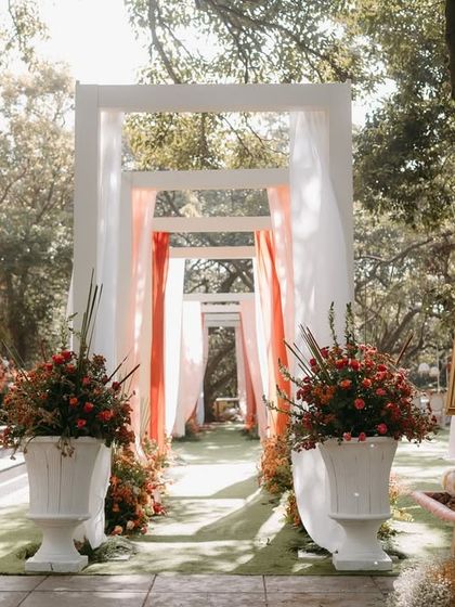 Soft hues, clean lines, and an effortless charm. This wedding entrance decor is pure, understated elegance, with white drapes and floral urns creating a serene and beautiful welcome.