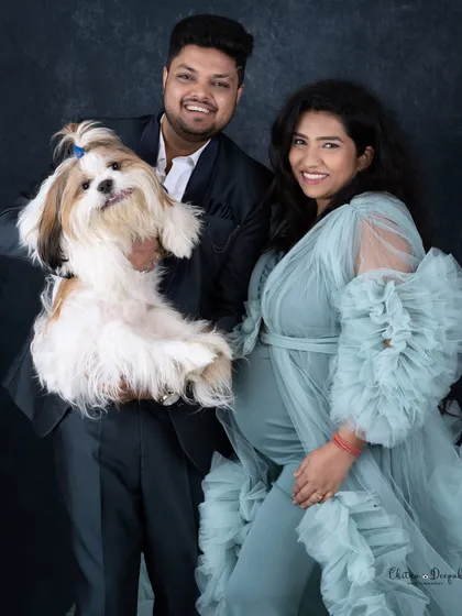 A smiling couple poses for a maternity portrait with their fluffy Shih Tzu, showcasing our pet-friendly studio environment.