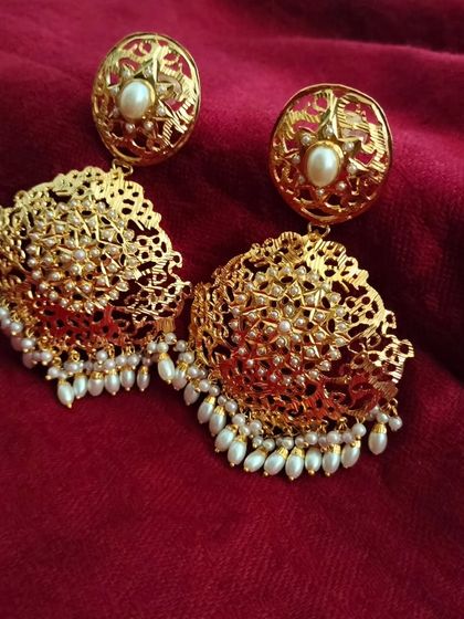 A close-up of the 'सेवंती' (Sevanti) earrings against a rich velvet background. The contrast highlights the gold plating and delicate pearl work.